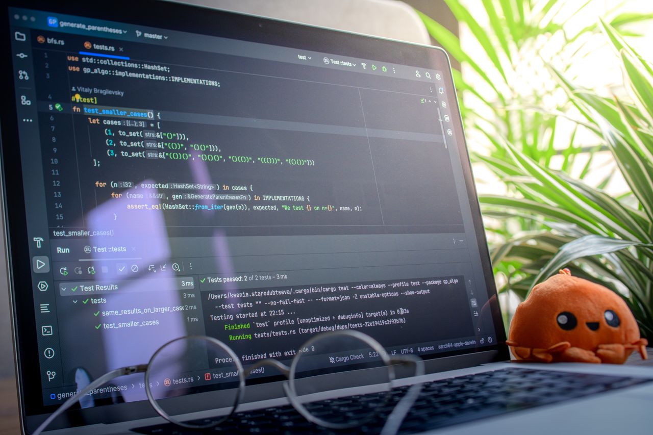 Open laptop displaying code next to a plush toy, set in a bright room with plants.